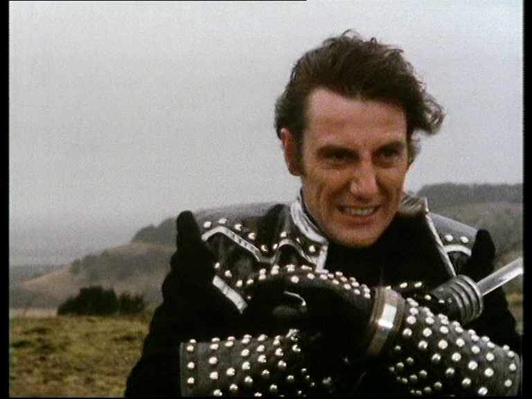 Avon grimacing against the wind, speaking into his teleport bracelet