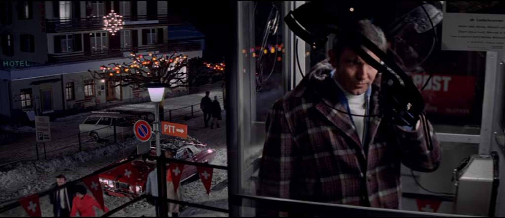 Bond inside a phonebox with Tracy's car in the background