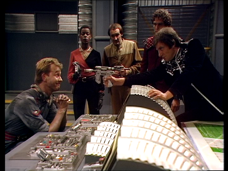 Avon leaning over a desk to point a gun at Dorian