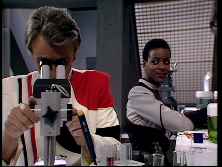 dayna smiling at justin as he peers through a microscope