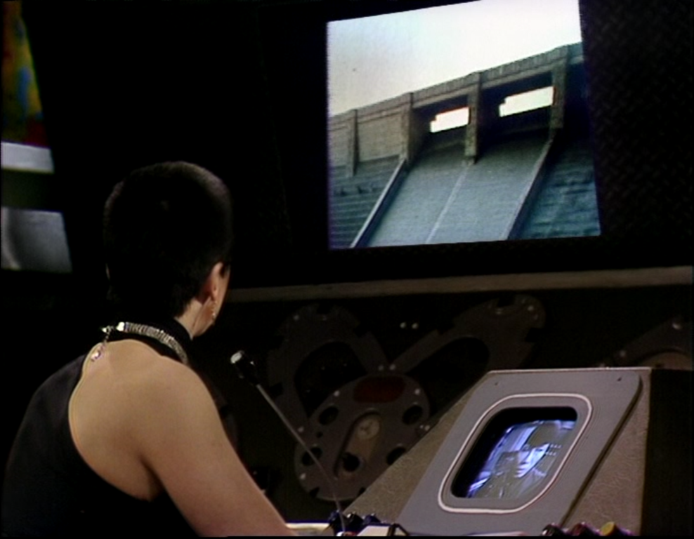 Servalan watches on a screen as the Liberator crew on a descend the dam's steps