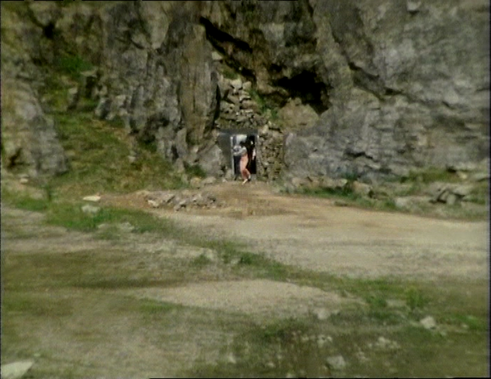Dayna and Tarrant emerging from a small door set in rocks