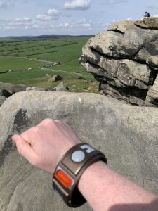 liberator bracelet on outstretched hand above rocks looking out across fields with sheep in