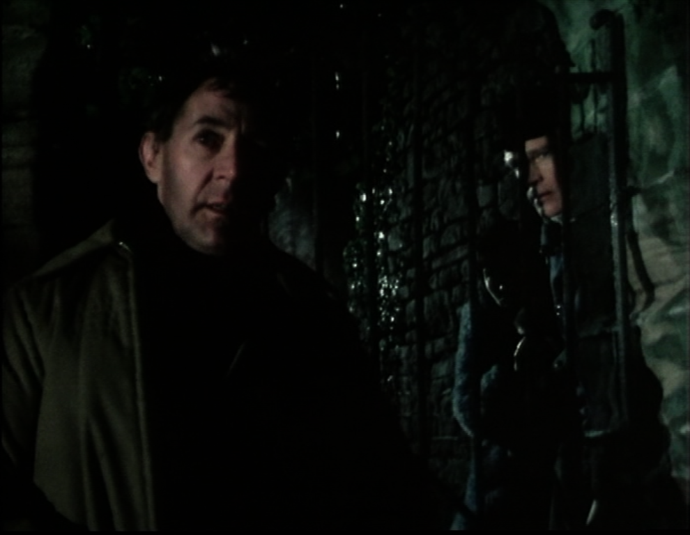 Robert Gillespie watches off camera for the return of the others while he whispers to Greg who is partially hiding in the shadows