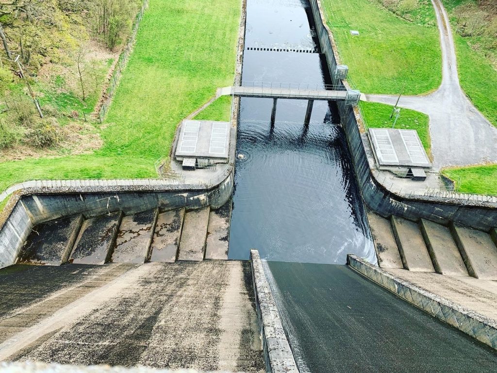 looking down over dam with river like pool of water and bridge below