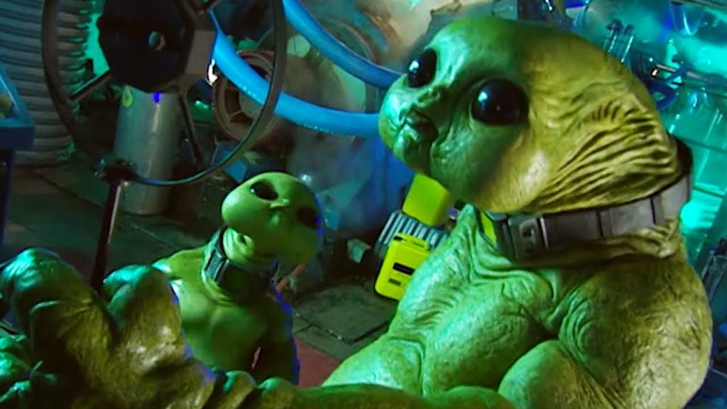 A child Slitheen looks up at an adult one as it speaks into an old fashioned microphone