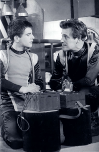 Gerald Flood in City Beneath the Sea, crouched with another man over diving equipment