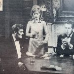 Miller and Lindale sit at a cards table with Caroline stood between them