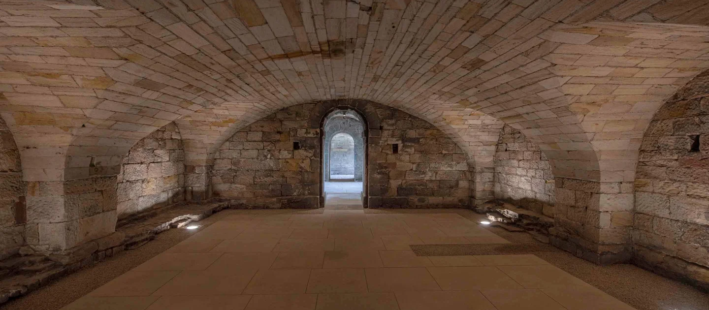 stone and brick basement with high alcoves and a door at one end leading to a lit corridor