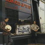 granny takes a trip storefront in 1966. two young men stand outside, one in a striped blazer, the other in a flowery shirt