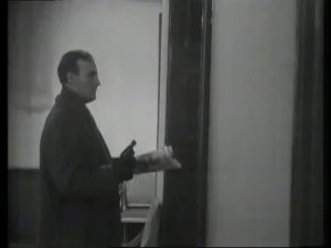 Callan looking out with newspaper in one hand and gun in the other